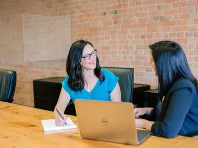 Zwei Frauen sitzen mit einem Laptop an einem Tisch und studieren Personalmanagement (B.A.).
