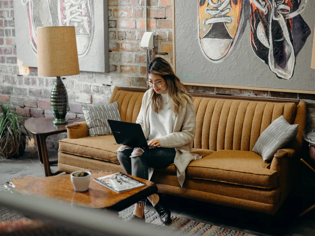 Eine Frau sitzt auf einem brauen Sofa und macht eine Weiterbildung in Social Media online mit ihrem Laptop