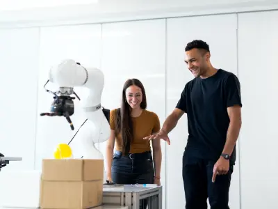 Zwei Studierende arbeiten mit einem weißen Roboterarm