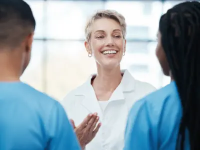 Eine lächelnde Ärztin im weißen Kittel spricht mit zwei Mitarbeitenden