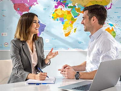 Zwei International Business Communication-Studierende unterhalten sich vor einer an der Wand hängenden Landkarte.