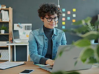 Frau mit Brille arbeitet am Laptop in modernem Büro