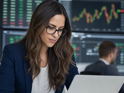 Finanzanalystin arbeitet am Laptop vor Börsenkursen.