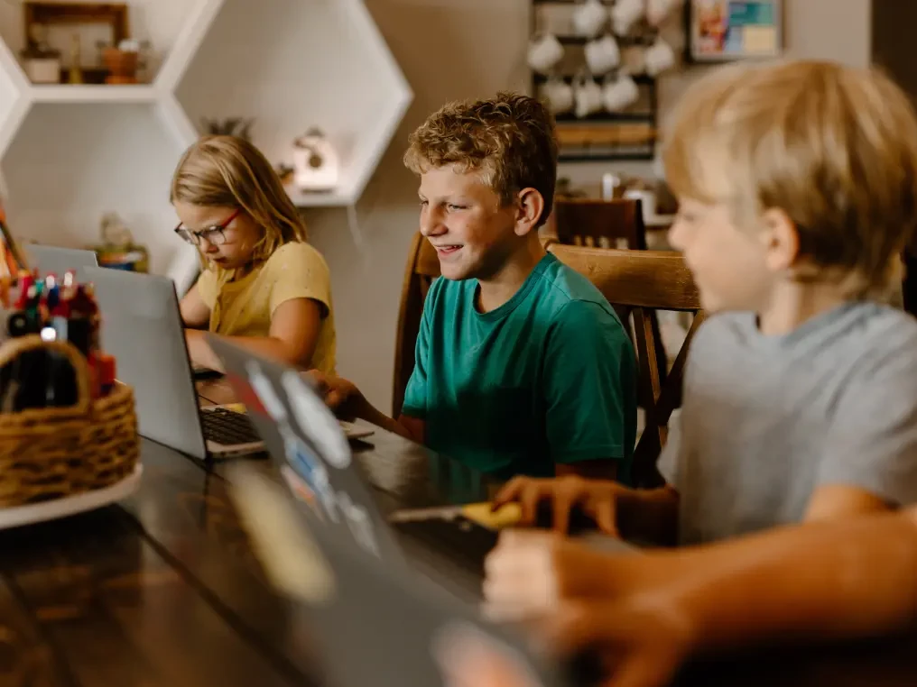 3 Kinder lernen zusammen an einem Tisch mit ihren Laptops