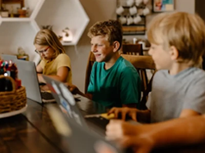 3 Kinder lernen zusammen an einem Tisch mit ihren Laptops