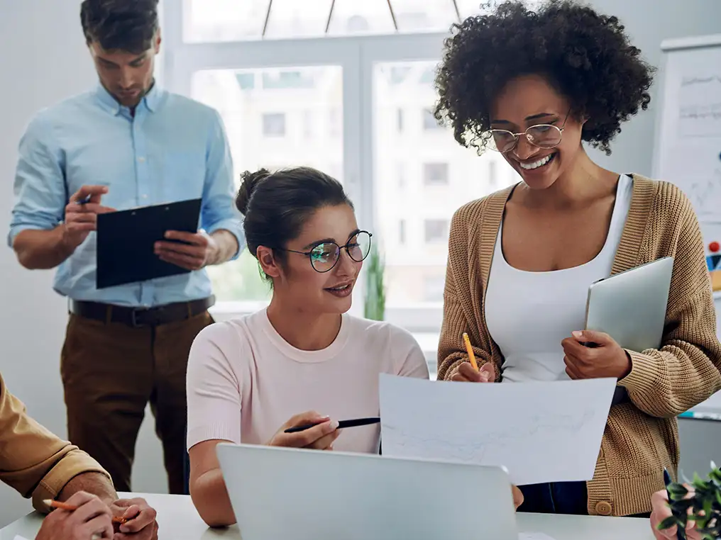 Vier Personen arbeiten gemeinsam in einem Büro an Dokumenten und einem Laptop.