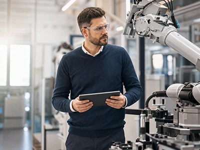 Techniker prüft mit einem Tablet einen Roboterarm in der Fertigung.