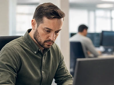 Mitarbeiter arbeitet konzentriert am Laptop im Großraumbüro.